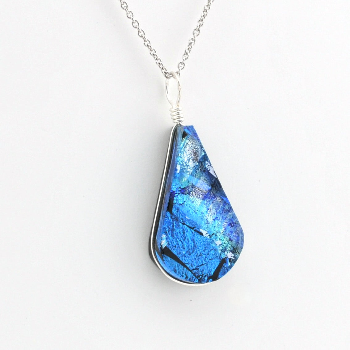 A teardrop-shaped blue iridescent dichroic glass pendant necklace with a silver bezel and chain, shown against a plain white background.