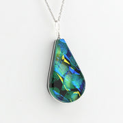A teardrop-shaped pendant necklace featuring a highly iridescent, color-shifting opal-like stone with vibrant green, blue, and yellow flashes, set in a silver bezel on a silver chain against a plain white background.