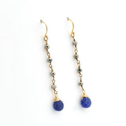 A pair of gold drop earrings with faceted beads and a teardrop-shaped blue lapis lazuli stone dangle, shown on a plain white background.