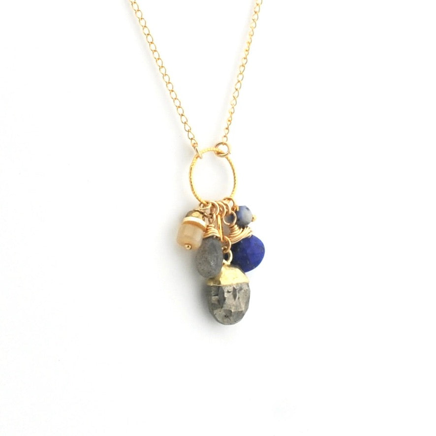 A gold chain necklace with a multi-charm pendant featuring natural stone beads in blue, gray, and beige, set against a plain white background.