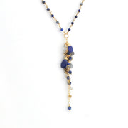 A gold-tone dangle necklace featuring a beaded chain with blue and gray beads, and a central cluster of polished blue stones and textured gold beads, shown against a plain white background.