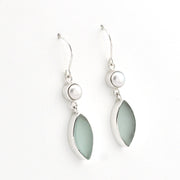A pair of silver dangle earrings featuring a small white pearl bead and a larger teardrop-shaped pale sea glass in a silver bezel setting, shown on a plain white background.