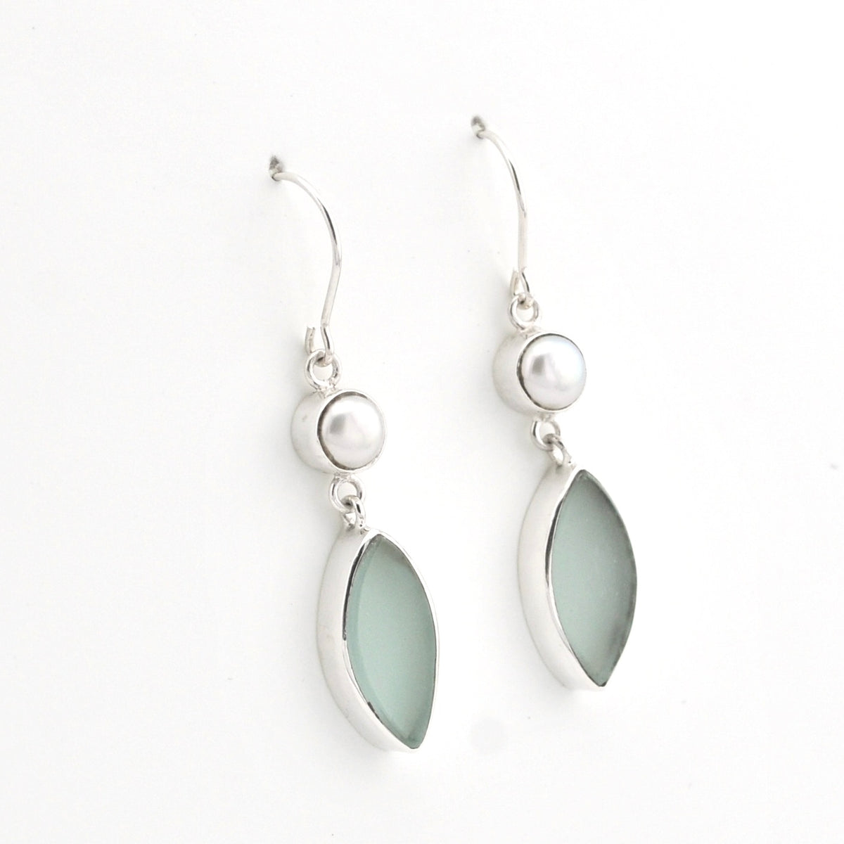A pair of silver dangle earrings featuring a small white pearl bead and a larger teardrop-shaped pale sea glass in a silver bezel setting, shown on a plain white background.