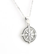 A silver compass pendant necklace with a central clear gemstone, shown on a delicate silver chain against a plain white background.