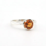 A silver ring featuring a round, faceted orange gemstone in a prong setting, shown on a plain white background.