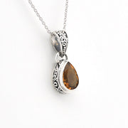 A silver pendant necklace featuring a teardrop-shaped citrine gemstone in an ornate silver bezel setting, suspended from a delicate silver chain against a plain white background.