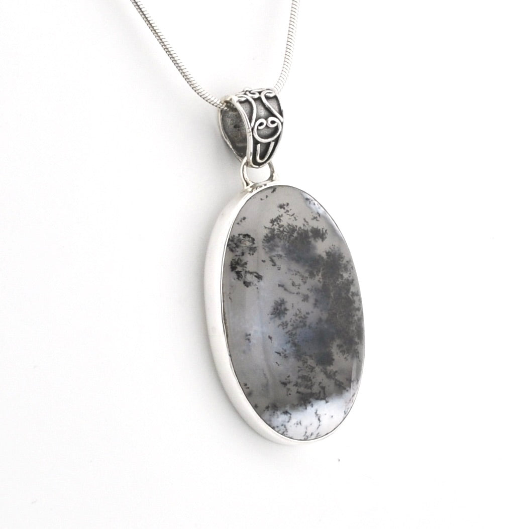 An oval pendant necklace featuring a gray and black marbled stone in a polished silver bezel, suspended from a silver snake chain against a plain white background.