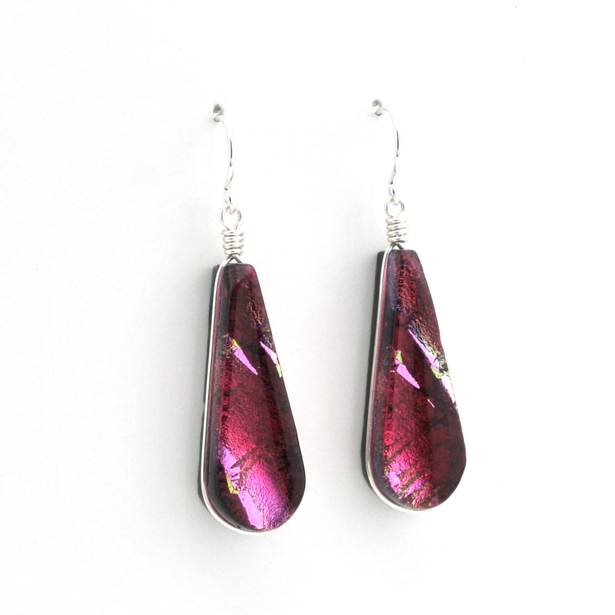 A pair of teardrop-shaped glass dangle earrings with a metallic pink and purple iridescent finish, suspended from silver fishhook wires on a plain white background.