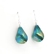 A pair of teardrop-shaped dangle earrings featuring iridescent green and blue dichroic glass in silver bezel settings with silver wire-wrapped hooks, shown on a plain white background.