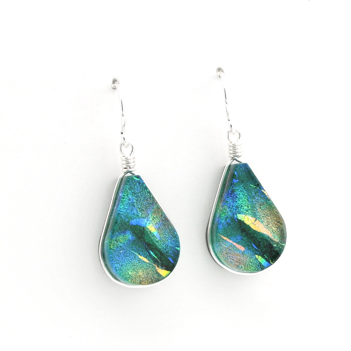 A pair of teardrop-shaped dangle earrings featuring iridescent green and blue dichroic glass in silver bezel settings with silver wire-wrapped hooks, shown on a plain white background.