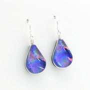 A pair of teardrop-shaped glass drop earrings with a vibrant blue, purple, and pink iridescent pattern, suspended from silver fishhook wires on a plain white background.