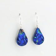 A pair of teardrop-shaped dangle earrings featuring vibrant blue iridescent dichroic glass set in silver bezel settings with silver fishhook wires, shown against a plain white background.
