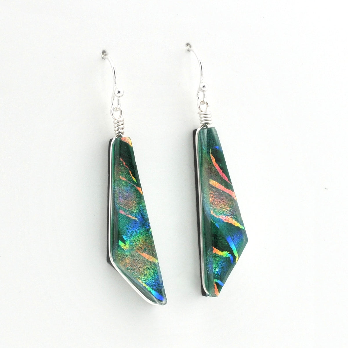 A pair of geometric drop earrings featuring iridescent green and blue dichroic glass set in silver, suspended from silver fishhook wires on a plain white background.