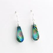 A pair of teardrop-shaped dangle earrings featuring iridescent green and blue dichroic glass in silver wire-wrapped settings with silver fishhook wires, shown on a plain white background.