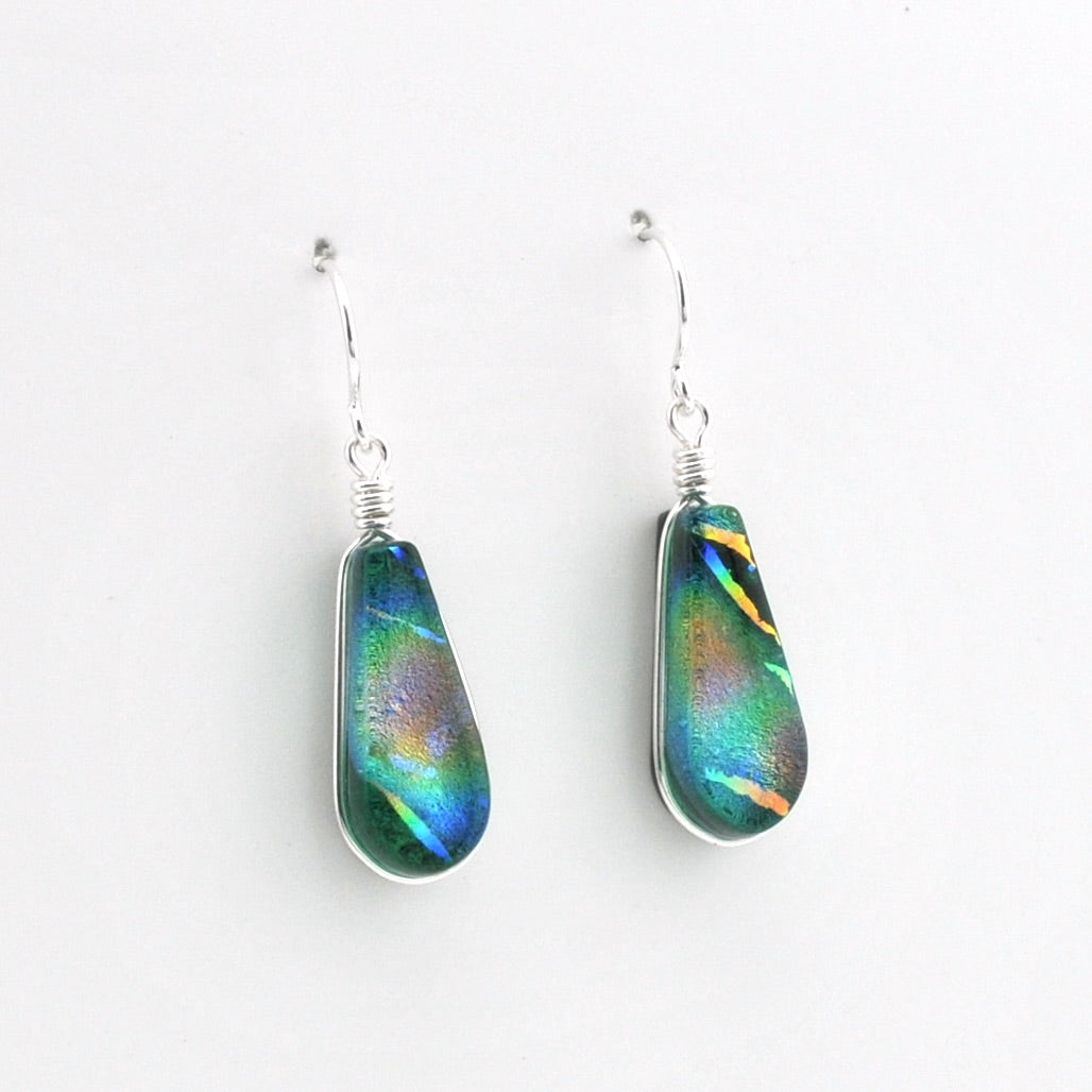 A pair of teardrop-shaped dangle earrings featuring iridescent green and blue dichroic glass in silver wire-wrapped settings with silver fishhook wires, shown on a plain white background.