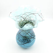 A light blue glass vase with a flared, ruffled rim and a rounded base, decorated with dark brown branch-like lines and green leaf details, set against a plain white background.