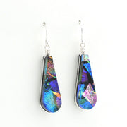 A pair of teardrop-shaped drop earrings featuring iridescent blue, purple, and green dichroic glass set in silver-tone metal with silver fishhook wires, shown against a plain white background.