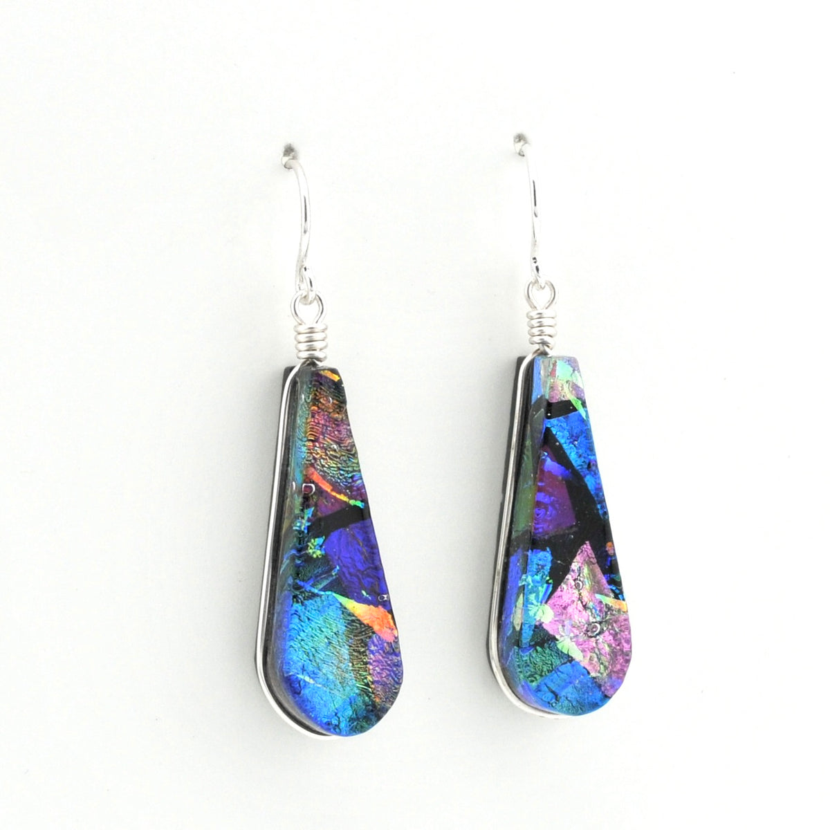 A pair of teardrop-shaped drop earrings featuring iridescent blue, purple, and green dichroic glass set in silver-tone metal with silver fishhook wires, shown against a plain white background.
