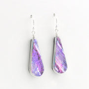 A pair of teardrop-shaped dangle earrings with silver wire-wrapped edges and hooks, featuring a marbled purple, pink, and blue iridescent dichroic glass shown against a plain white background.