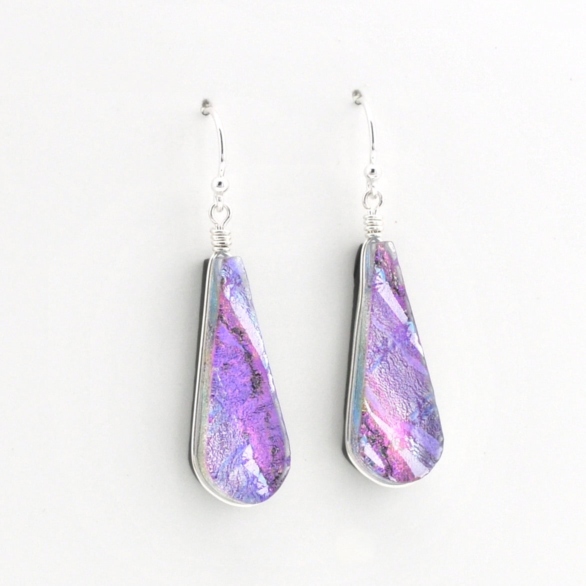 A pair of teardrop-shaped dangle earrings with silver wire-wrapped edges and hooks, featuring a marbled purple, pink, and blue iridescent dichroic glass shown against a plain white background.