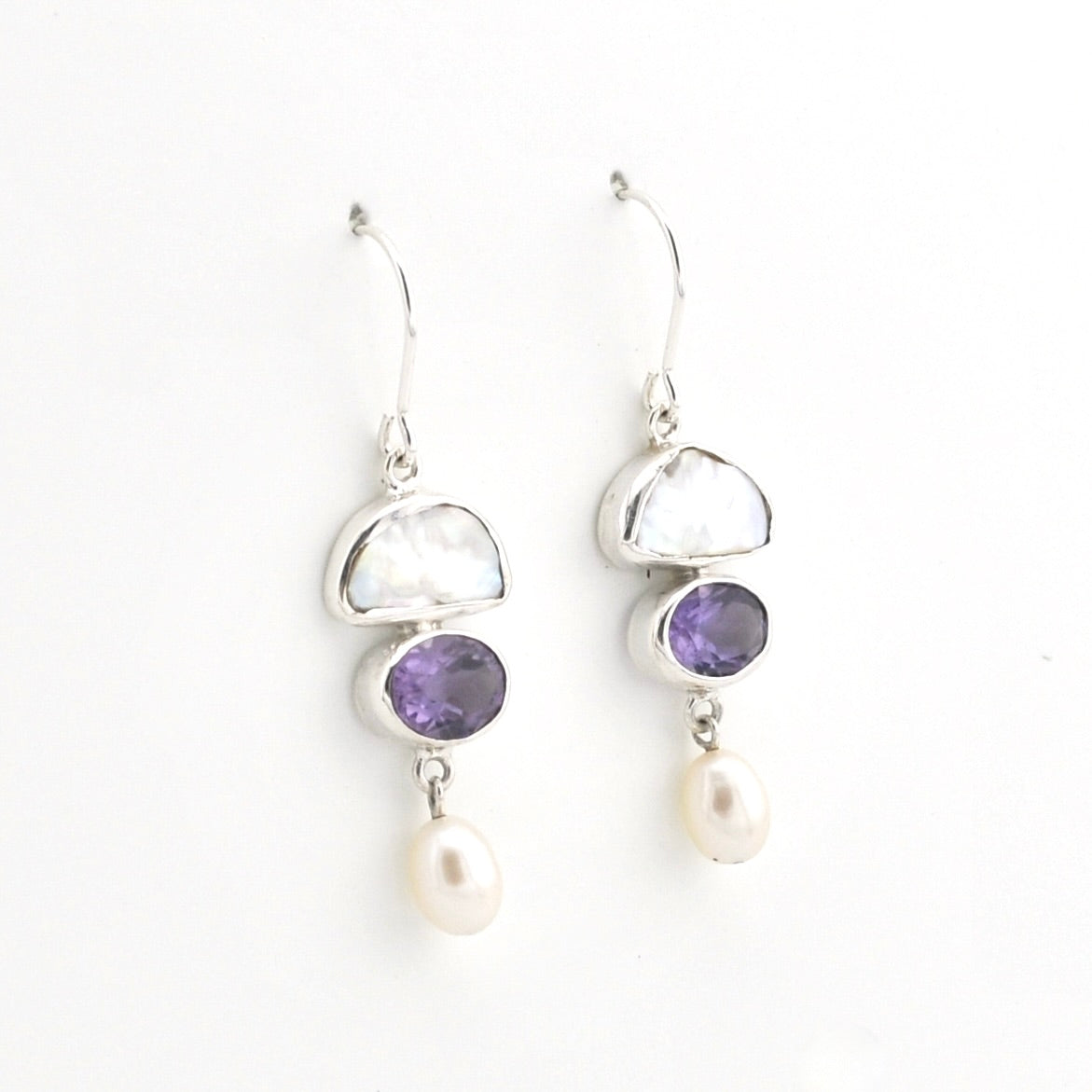 A pair of silver drop earrings featuring a white mother-of-pearl crescent, a purple amethyst oval, and a dangling white pearl, shown on a plain white background.