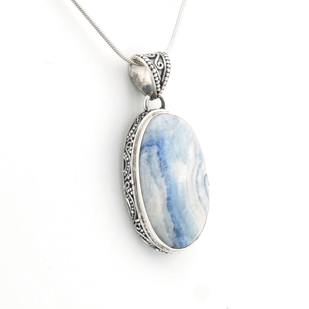 A silver pendant necklace featuring an oval cabochon stone with natural light blue and white marbled patterns, set in an ornate silver bezel on a delicate silver chain.