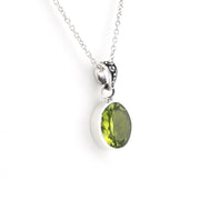 A silver pendant necklace featuring an oval-cut green gemstone in a silver bezel setting, suspended from a delicate silver chain against a plain white background.
