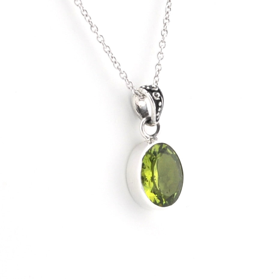 A silver pendant necklace featuring an oval-cut green gemstone in a silver bezel setting, suspended from a delicate silver chain against a plain white background.
