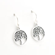 A pair of silver tree of life drop earrings with circular cutout pendants and fishhook wires, shown on a plain white background.
