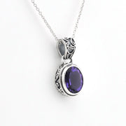 A silver pendant necklace featuring an oval-cut deep purple gemstone in an ornate silver bezel setting, suspended from a delicate silver chain against a plain white background.