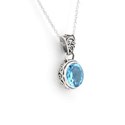 A silver pendant necklace featuring an oval-cut light blue gemstone in an ornate filigree bezel setting, suspended from a delicate silver chain against a plain white background.
