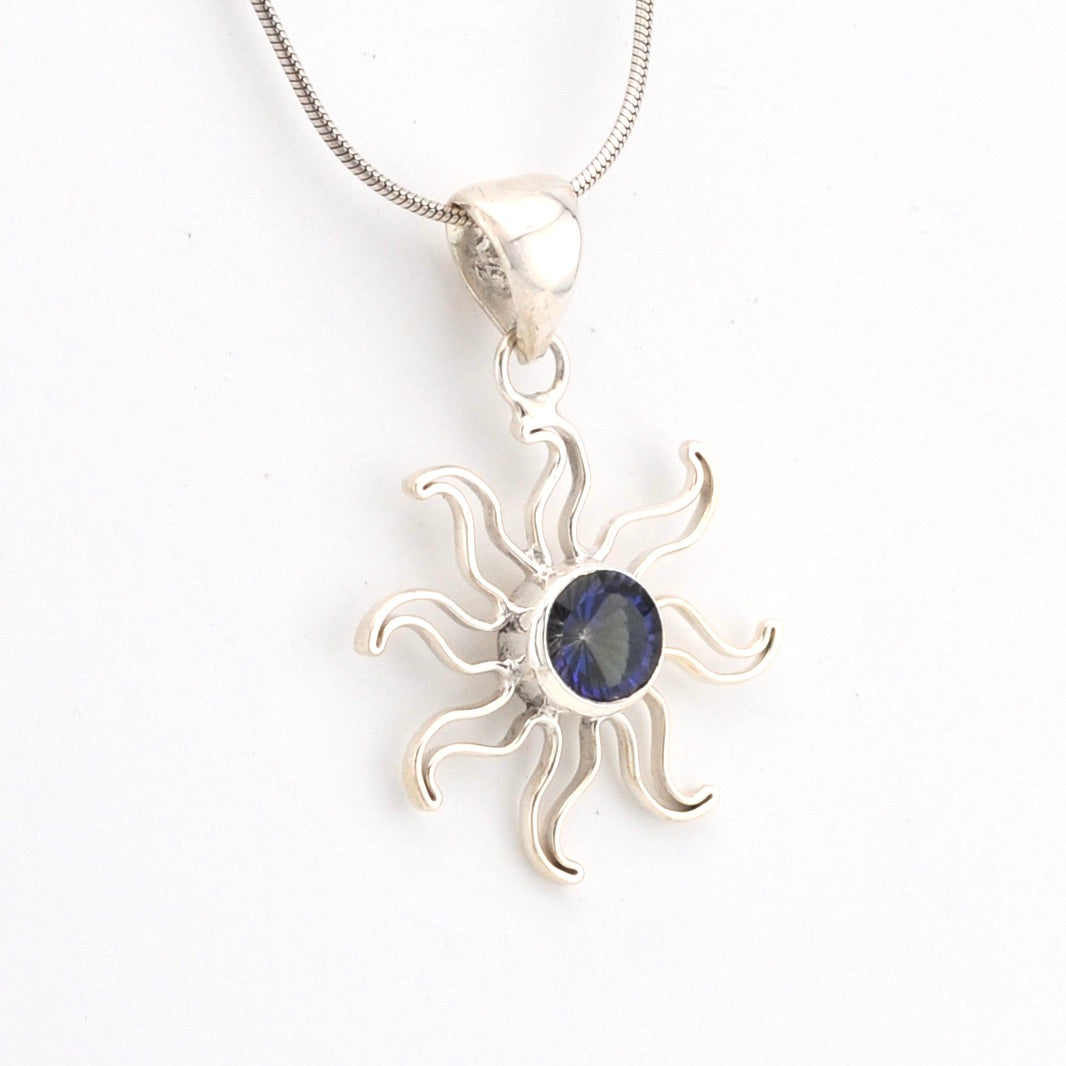 Silver sun-shaped pendant with a blue gemstone on a white background