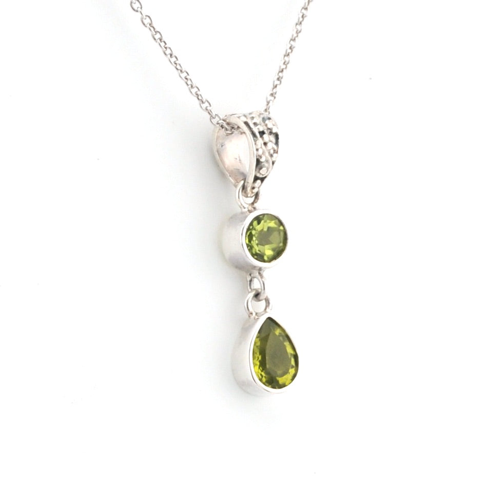 Silver necklace with green teardrop pendant on a white background