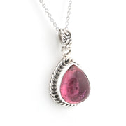 A silver pendant necklace featuring a teardrop-shaped pink gemstone in a textured, rope-style silver bezel setting, suspended from a delicate silver chain against a plain white background.