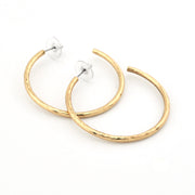 A pair of gold hoop earrings with a textured, hammered finish, shown on a plain white background.