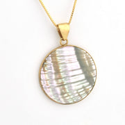 Necklace with a round, shell-like pendant on a gold chain against a white background