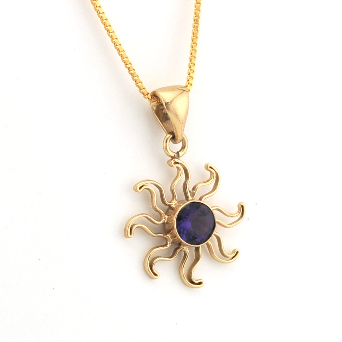 Gold sun-shaped pendant with a purple gemstone on a white background