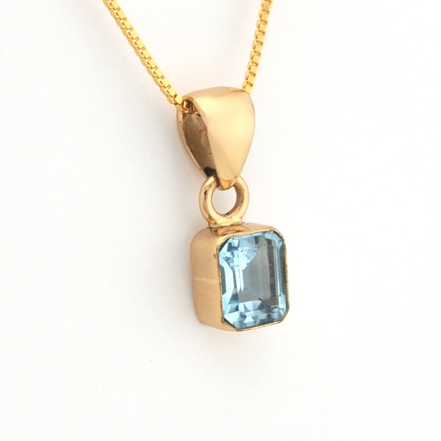 Gold pendant with a blue gemstone on a white background