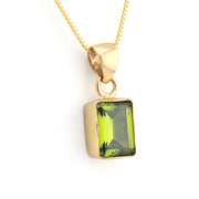 A gold pendant necklace featuring a rectangular green gemstone, shown against a plain white background.