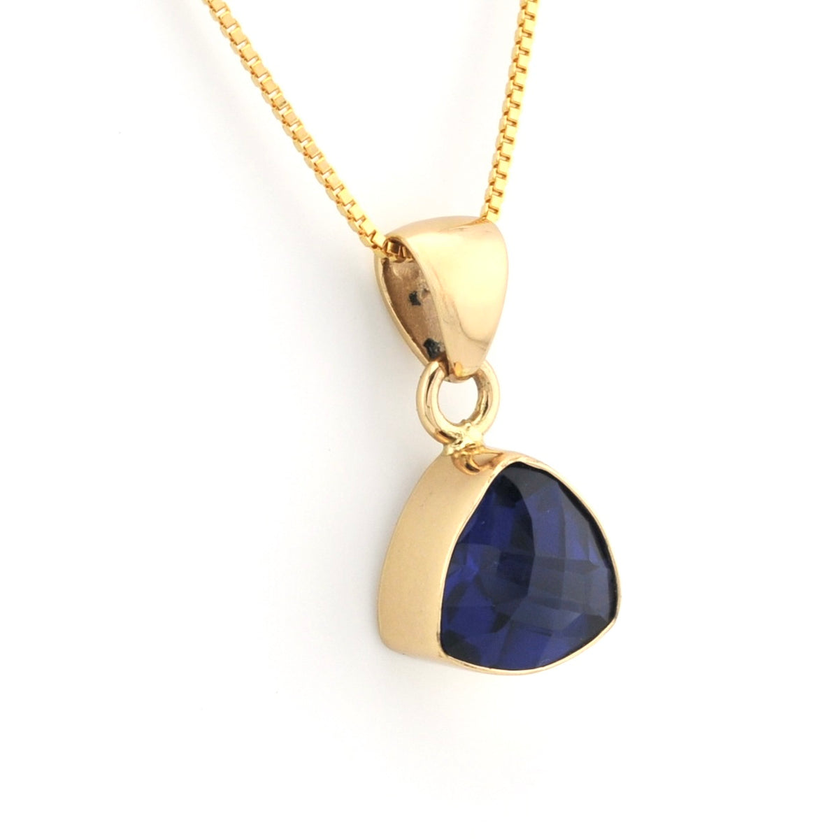 A gold pendant necklace featuring a faceted, teardrop-shaped dark blue gemstone in a gold bezel setting, suspended from a gold chain against a plain white background.