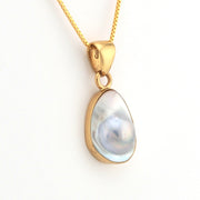 Gold pendant with a teardrop-shaped gemstone on a white background