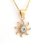 Gold sun-shaped pendant with a central gemstone on a white background