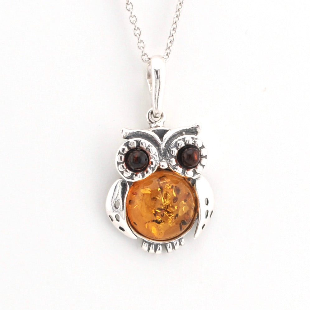 Silver owl pendant with amber center and brown stones on a white background