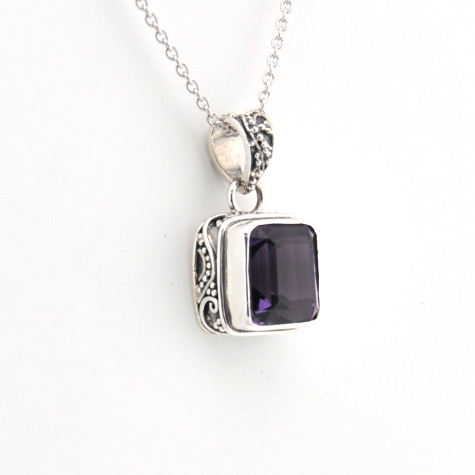 Silver pendant with a purple gemstone on a white background