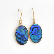 Gold earrings with blue paua shell drops on a white background