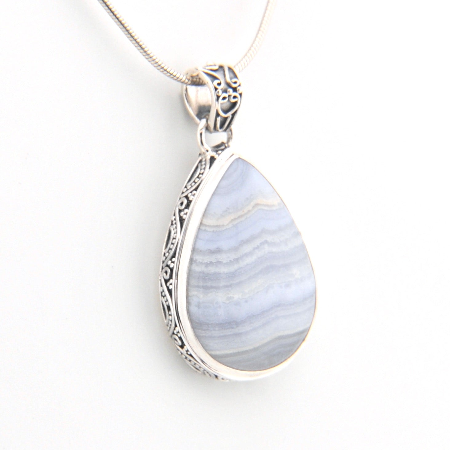 Teardrop-shaped pendant with blue and white marbled stone and silver frame on a white background
