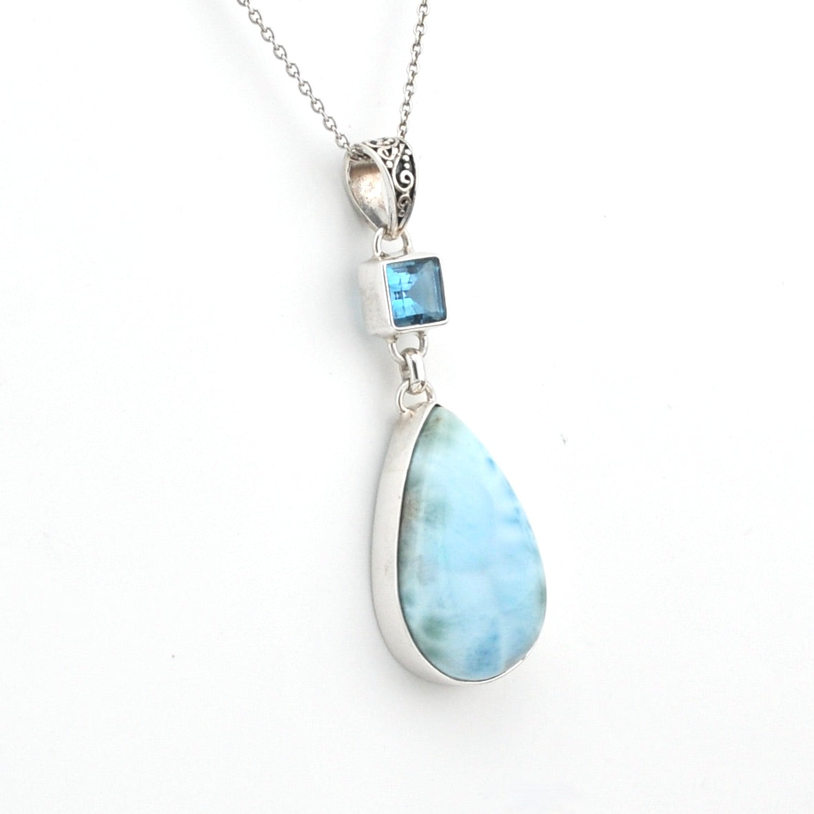Teardrop-shaped larimar pendant with blue topaz on a white background