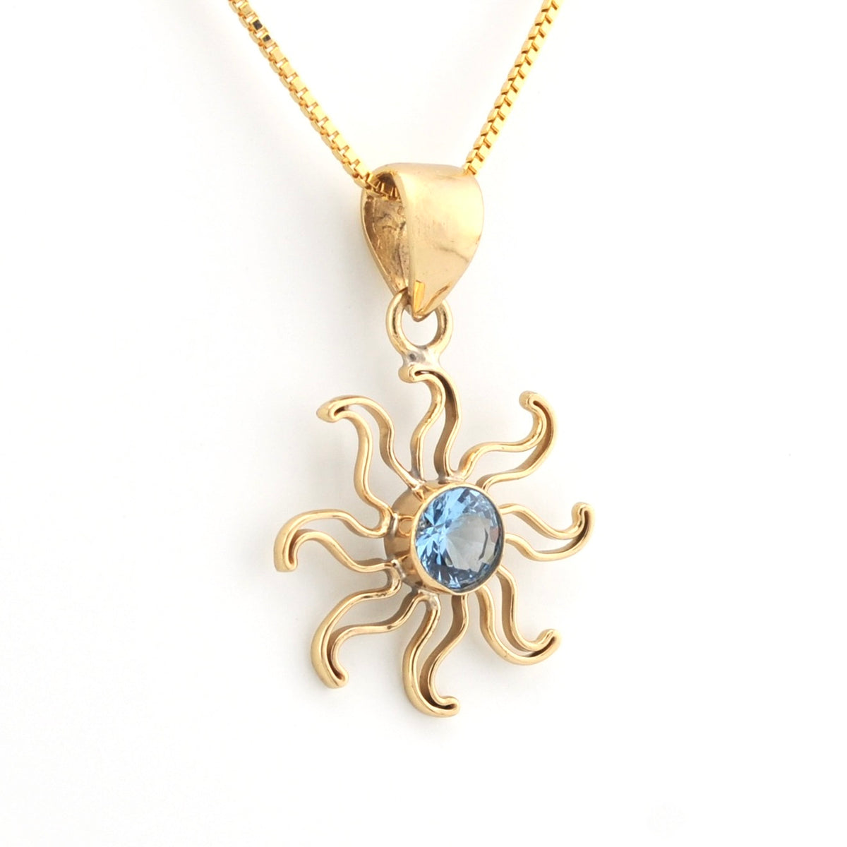 A gold pendant necklace featuring a stylized sun design with a central light blue gemstone, shown on a clean white background.