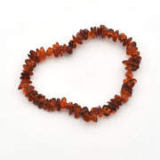 A handmade beaded bracelet made of polished, irregular amber chips in warm reddish-brown and orange tones, arranged in a circle on a plain white background.