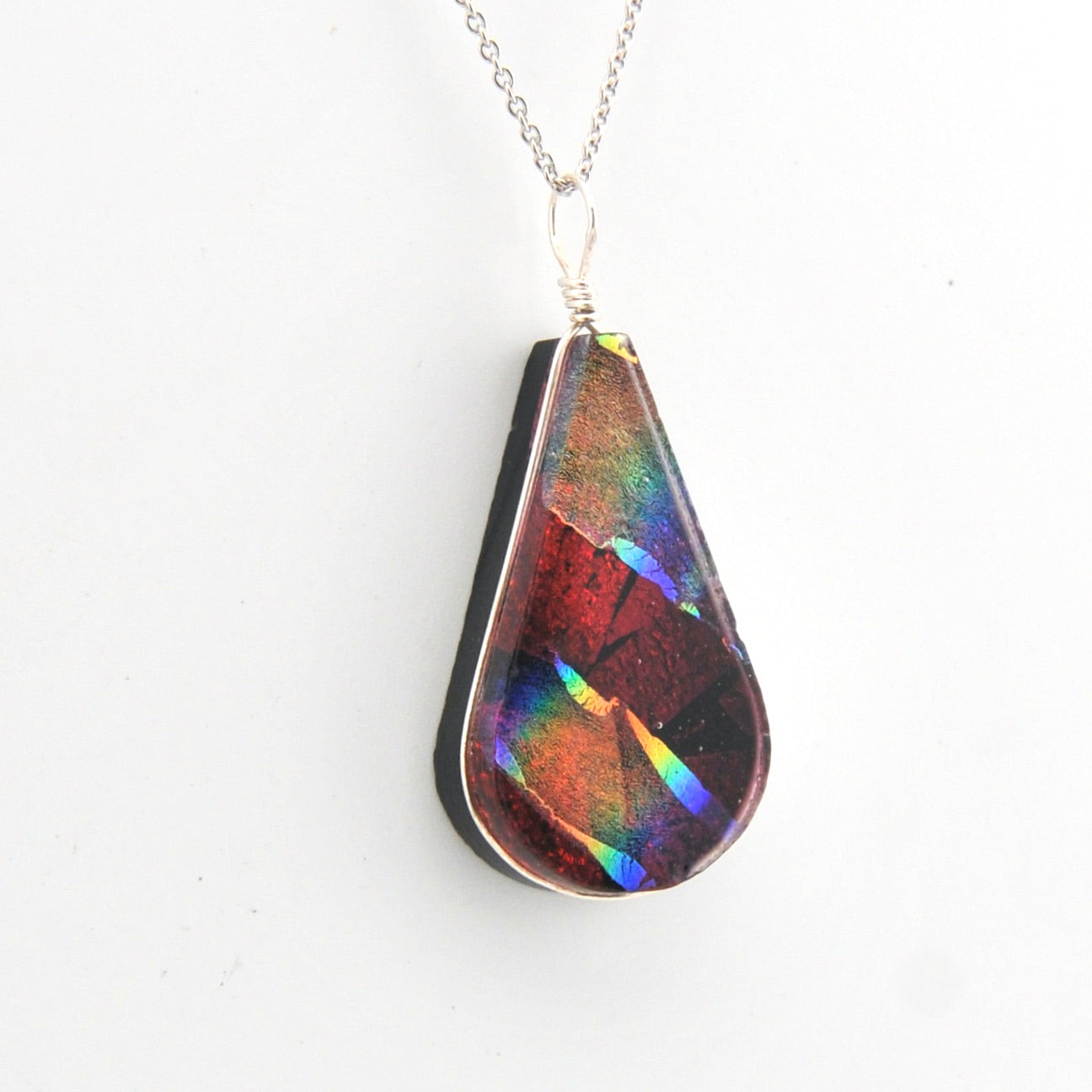 Teardrop-shaped pendant with multicolored iridescent surface on a white background